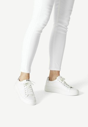 Baskets blanches avec un motif texturé en nid d'abeille. Elles présentent un bout arrondi, une semelle plate et des lacets blancs, associées à un jean slim blanc.