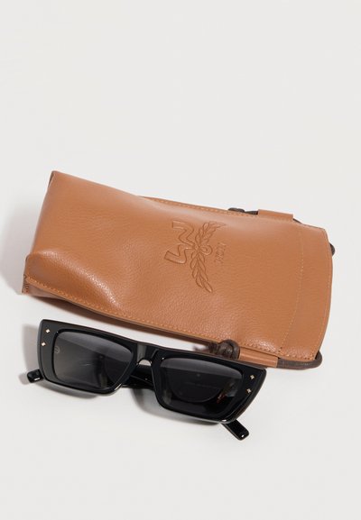 Μαύρα ορθογώνια γυαλιά ηλίου με μικρές χρυσές λεπτομέρειες τοποθετημένα μπροστά σε καφέ δερμάτινο πουγκί με κορδόνι και ανάγλυφο λογότυπο.