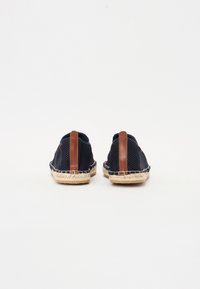 Baskets slip-on en maille marine avec accents de talon en cuir marron, dotées d'une semelle en jute tissé pour une texture et des détails supplémentaires.