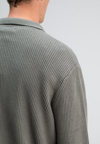 Geribbelde grijze cardigan met een kraaghals. De textuur is zacht en gebreid, met een ontspannen pasvorm en zichtbare stiknaden.