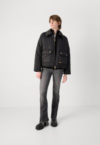 Casaco acolchoado preto com dois bolsos frontais e detalhamento em tom dourado. Combinado com jeans cinzentos desgastados e botas pretas de plataforma volumosa.