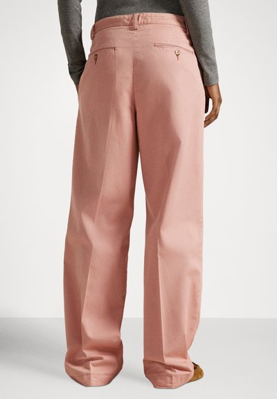 Spodnie o szerokich nogawkach wykonane z miękkiej różowej tkaniny, z wysokim stanem, tylnymi kieszeniami ozdobionymi dekoracyjnymi elementami oraz luźnym krojem.
