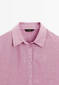 Chemise en lin violet clair avec col et boutons sur le devant, présentée à plat sur un fond blanc.