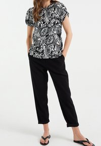 Černobílé květinové tričko s krátkým rukávem v kombinaci s černými úzkými kalhotami, které mají ohrnuté manžety, a černými žabkami.