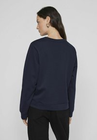 Jūrinės mėlynai pilkos spalvos crewneck tipo megztinis su ilgomis rankovėmis, laisvu kirpimu ir raukinėtu apvadu. Tekstūruotas audinys su lygia apdaila, be matomų raštų ar logotipų.