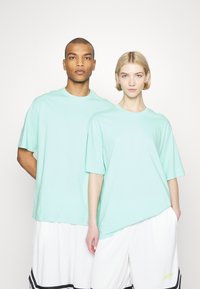 Menta zöld, oversized rövid ujjú pólók, kerek nyakkivágással és puha anyagból, laza fehér sorttal viselve, fekete akcentussal.