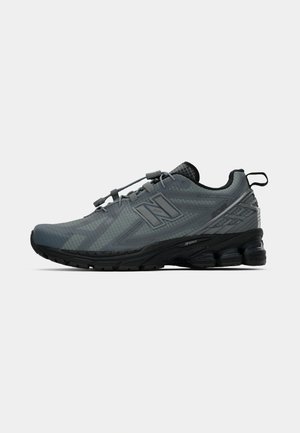 Scarpa da corsa grigia con tomaia in mesh testurizzato, loghi distintivi, lacci elastici e suola imbottita con tasche d'aria visibili.