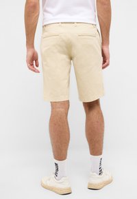 Shorts en chino beige à coupe droite, avec un design de poche arrière et un ourlet propre. Portés avec des sneakers blanches et des chaussettes à motifs.