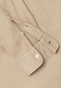 Μανίκι πουκαμίσου από μπεζ λινό με μανσέτα με κουμπιά, που δείχνει τρύπες για κουμπιά και λεπτομέρειες ραφής σε υφασμένο ύφασμα.