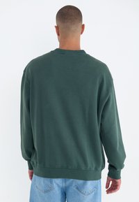 Groene oversized sweatshirt van een katoenmix, met een ronde hals en ribgebreide manchetten, gecombineerd met lichtblauwe spijkerbroek.