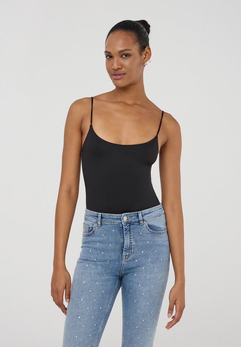 Body nero con spalline sottili abbinato a jeans chiari a vita alta con decorazioni in perle, creando una silhouette aderente.
