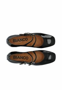 Zapatos de charol negros con punta cuadrada, dos tiras finas ajustables y una plantilla marrón con el nombre de la marca "BIANCO."
