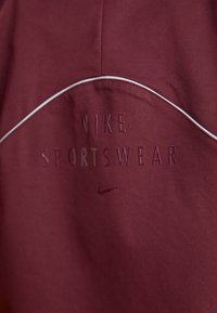 Vestuário desportivo Nike na cor bordeaux com texto elevado e uma costura de destaque branca. Textura suave com um design ajustado.