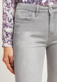 Vaqueros de mezclilla gris con una textura suave, diseño de cinco bolsillos y detalles de costura sutiles, combinados con una blusa de estampado floral.