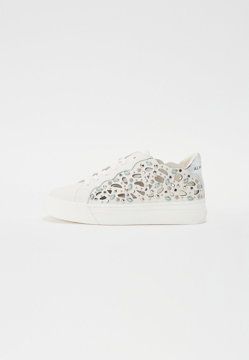 Hvit sneaker med utskårne blomsterdesign i blå og sølv aksenter. Myk tekstur med snøring, flat såle og avrundet tå.