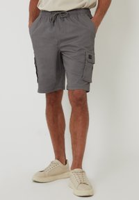 Pantalones cortos cargo grises con cintura elástica y cordón, que cuentan con bolsillos laterales y un bolsillo de parche en la pierna. Textura de tela suave.