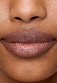 Rossetto opaco color malva su labbra lisce e ben definite, che mostrano una consistenza morbida con linee sottili. Messa a fuoco ravvicinata sull'area della bocca.