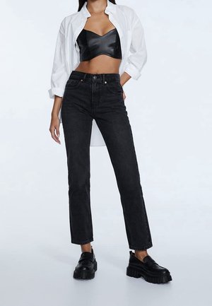 Jean en denim noir avec une coupe droite, taille haute et texture subtilement délavée. Associé à un bustier en cuir noir et une chemise blanche.