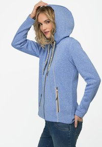 Blå hoodie i texturerat material, med en framficka med dragkedja, två sidofickor med dragkedjor och en huva med snodd.