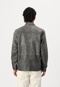 Giacca di pelle grigia con una texture liscia, cuciture strutturate e colletto piatto, abbinata a pantaloni chiari.