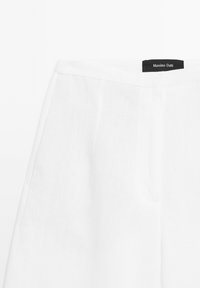 Weiße Leinenhose mit glatter Textur, seitlichen Taschen und einem gestickten Bund. Das Etikett "Massimo Dutti" ist angebracht.