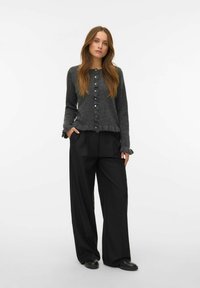 Tmavě šedý pletený cardigan s zapínáním na knoflíky a volánkovým lemem, kombinovaný s černými širokými kalhotami a černými slip-on botami.