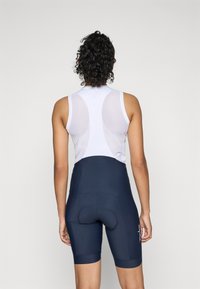 Cykeloutfit bestående af en hvid mesh-ryg uden ærmer og marineblå shorts med polstret sæde og logo detaljer på siden.