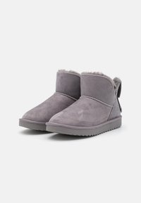 Bottines en suède gris avec une douce doublure en fourrure, semelles en caoutchouc plates et détails cousus sur le dessus. Comprend un petit onglet à l'arrière.