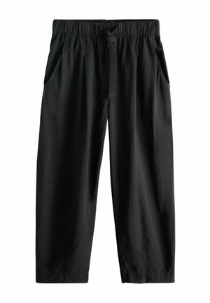 Woman standing wearing loose black pants, beige knit top, wooden beaded bracelet, and brown sandals, shown from the back.