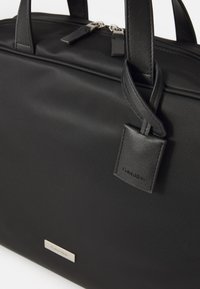Zwarte nylon tote bag met leren accenten, ritssluiting, dubbele handvatten en een klein merkaafbeelding. Heeft een gladde, matte afwerking.