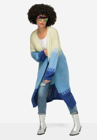 Cardigan lavorato a maglia in crema, azzurro chiaro e blu scuro, con motivi geometrici. Abbinate a jeans chiari e stivaletti ankle in argento.