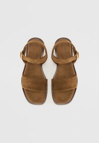 Bruna mockaskor med två breda remmar och en spänne. Sulan är platt med en lätt kurva, har en slät yta och en enkel design.