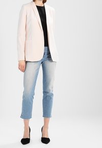 Jasnoróżowa marynarka o dopasowanym kroju, z zapięciem na jeden guzik i dwoma przednimi kieszeniami. Do tego jasnoniebieskie, skrócone jeansy i czarne szpilki.