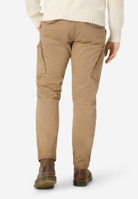 Beige Cargohosen mit zwei Seitentaschen, zulaufenden Beinen und einer glatten Baumwollstruktur. Kombiniert mit braunen Stiefeln und einem cremefarbenen Pullover.