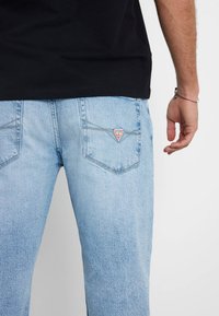 Jeans in denim azzurro chiaro con una vestibilità comoda, con una toppa triangolare rossa del marchio Guess sulla tasca posteriore destra e un leggero effetto sbiadito.