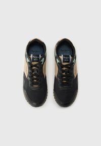 Černé a hnědé nízké tenisky se strukturovaným koženým svrškem, kulatými tkaničkami, mintově zelenými detaily a kontrastním logem na jazyku.