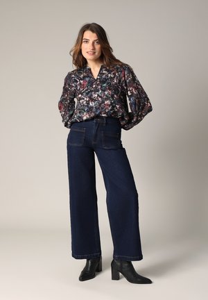 Blouse à manches longues transparente avec un motif floral et un décolleté en V, associée à un jean large taille haute bleu foncé et des bottines noires.