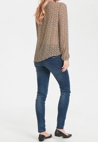 Brun mönstrad blus med diamantdesign, kombinerad med mörkblå tajta jeans och svarta flats. Långärmad, avslappnad passform på blusen.