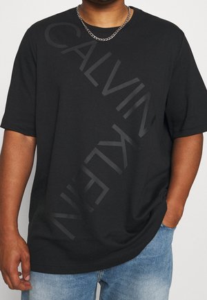 T-shirt en coton noir avec un grand logo "CALVIN KLEIN" ton sur ton en diagonale sur le devant. Manches courtes et coupe décontractée.