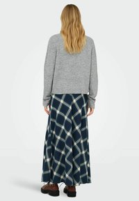 Suéter de punto gris, falda maxi de cuadros azul de talle alto con líneas blancas y verdes, rematada con botas marrones con cordones.