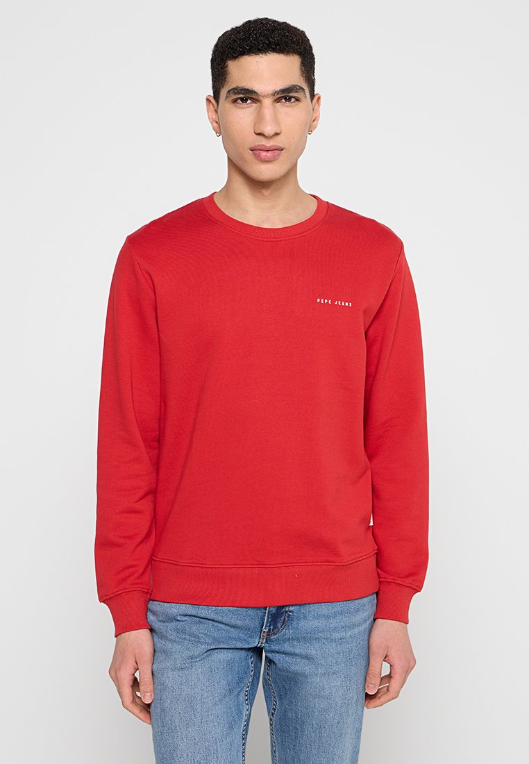Roter Baumwollpullover mit Rundhalsausschnitt, langen Ärmeln und Rippbündchen. Mit einem kleinen weißen Logo auf der linken Brust. Klassische Passform.