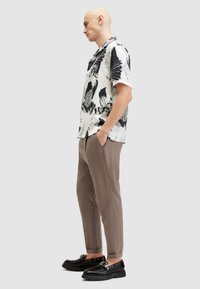 Camisa de manga corta en blanco con patrón abstracto negro, combinada con pantalones beige. Calzado negro con suela gruesa y detalle de hebilla.