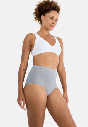 Donna con capelli ricci che indossa un reggiseno wireless bianco e una mutanda a vita alta grigio chiaro senza cuciture, in piedi davanti a uno sfondo semplice.