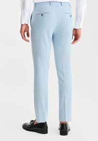 Jasnoniebieskie dopasowane spodnie o slim fit, z dwiema tylnymi kieszeniami i gładką teksturą. Połączone z czarnymi butami, widok z tyłu.