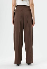 Pantalon marron taille haute avec une coupe pattes d’éléphant, devant plat et deux poches arrière. Confectionné dans un tissu lisse avec un léger éclat.