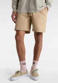 Beige shorts med snoretræk i taljen, parret med lyserøde ankelsokker med sort skrift og brune sneakers med hvide såler.