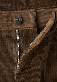 Pantalones de pana marrón con una cremallera plateada visible y un botón de metal negro, que muestran una textura acanalada y un diseño de bolsillo estándar.