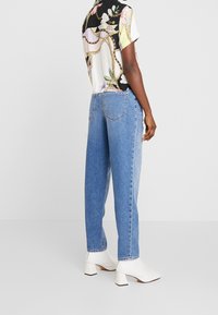 Blus med blommönster och kort ärm i svart, krämfärgad och pastellfärger, ihop med ljusblå vida jeans och vita klackade ankelskor.