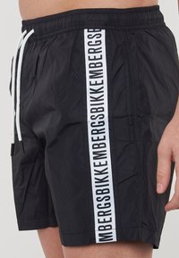 Shorts da nuoto neri realizzati in materiale leggero. Dotati di un elastico in vita, cordino bianco e una striscia con logo a contrasto audace.