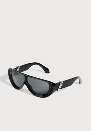 Lunettes de soleil noires avec des verres gris foncé, une monture épaisse aux formes sculptées et des détails décoratifs argentés sur les branches.